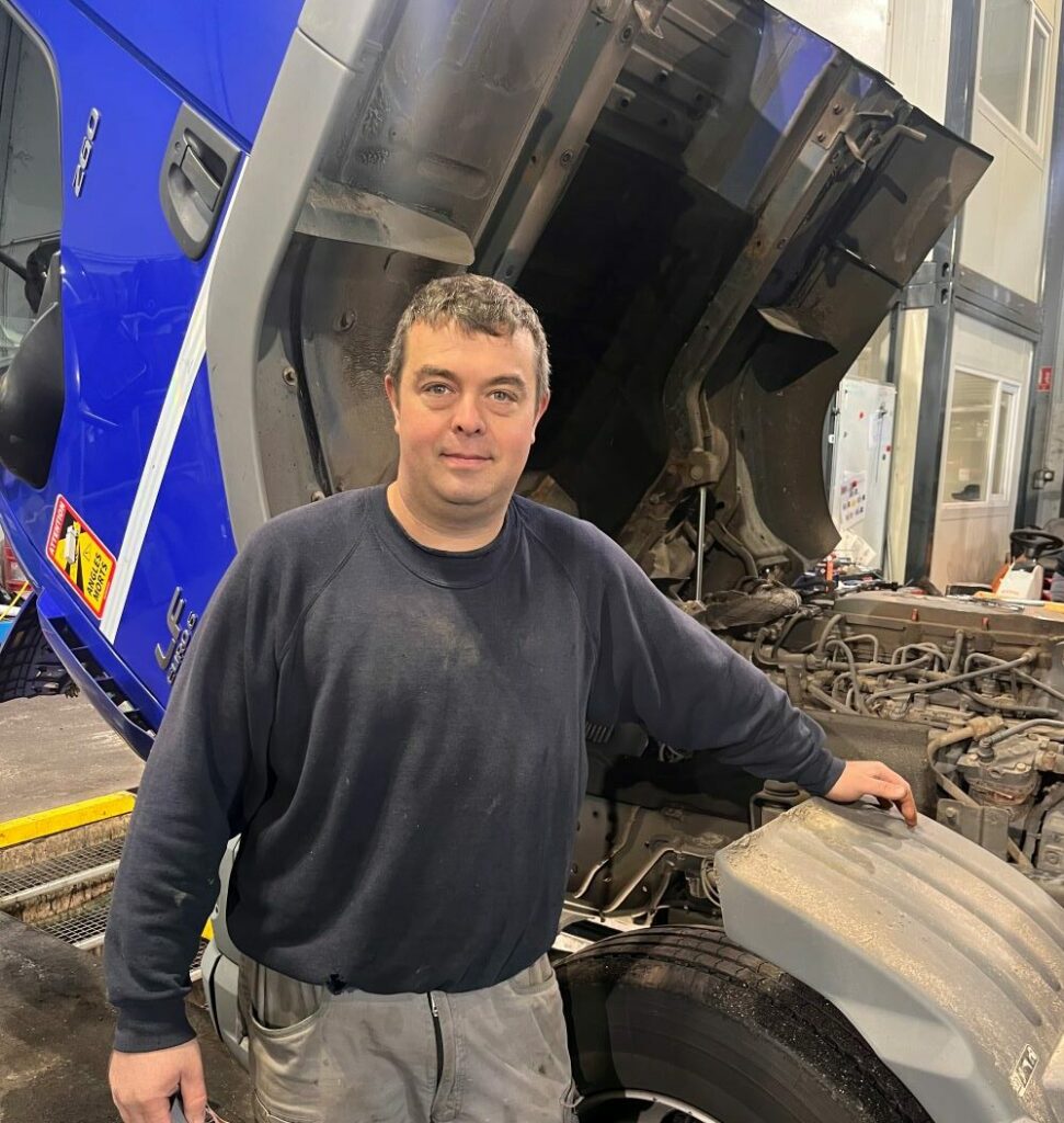 Julien, notre chef d'atelier devant un moteur de camion, nous expliquant une de ses journées types